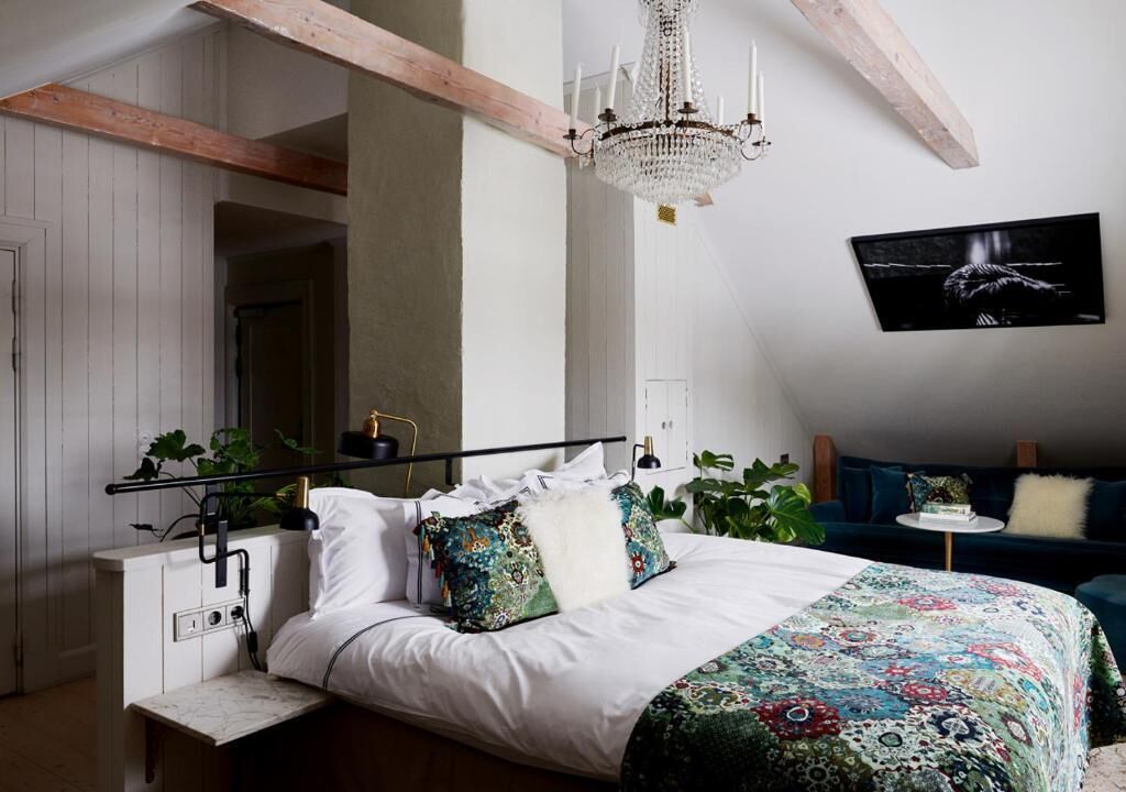 A bedroom with a bed, a chandelier, a wall-mounted TV, and a bedside table with a lamp.