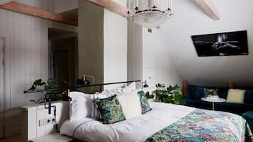A bedroom with a bed, a chandelier, a wall-mounted TV, and a bedside table with a lamp.