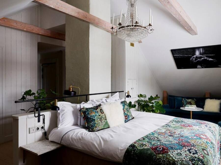 A bedroom with a bed, a chandelier, a wall-mounted TV, and a bedside table with a lamp.
