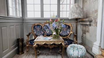 Ein Zimmer mit einem alten Sofa, einem kleinen Tisch mit Blumen in einer Vase und einer dekorativen Lampe.