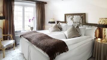 A bedroom with a large bed, two bedside lamps, a chair, and a window with curtains.