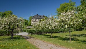 A large building with a stone facade, surrounded by a well-maintained garden with blooming trees and a gravel path. - Görvälns Slott (Jarfalla)