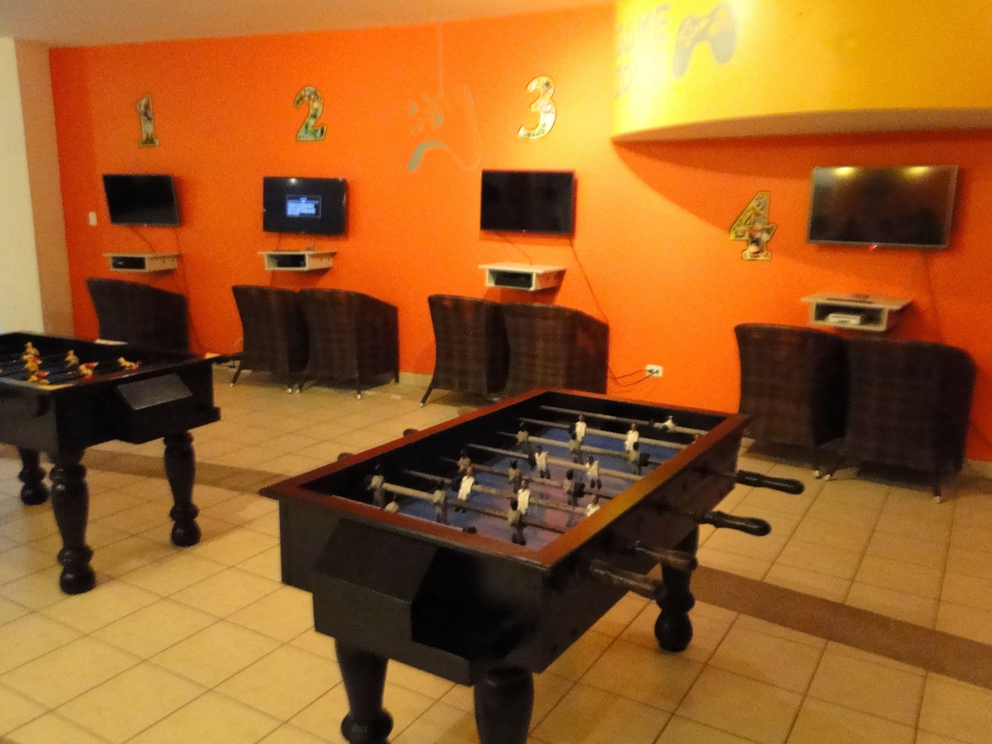 A room with two foosball tables, a pool table, and four sofas.
