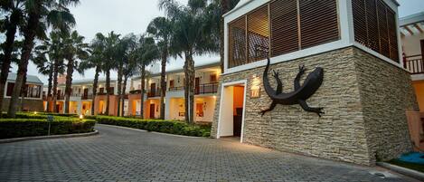 A hotel entrance with a paved driveway, palm trees, and a building with a stone facade and a number sign.