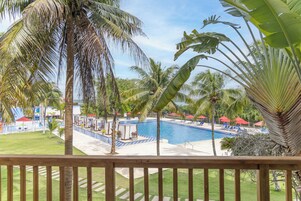 Un área de piscina con palmeras, sillas de descanso y sombrillas.