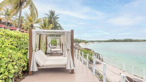 A wooden deck with a canopy bed overlooking a beach.