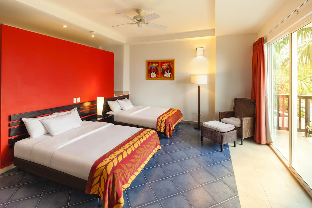 A hotel room with two beds, a chair, a lamp, and a large window with curtains.