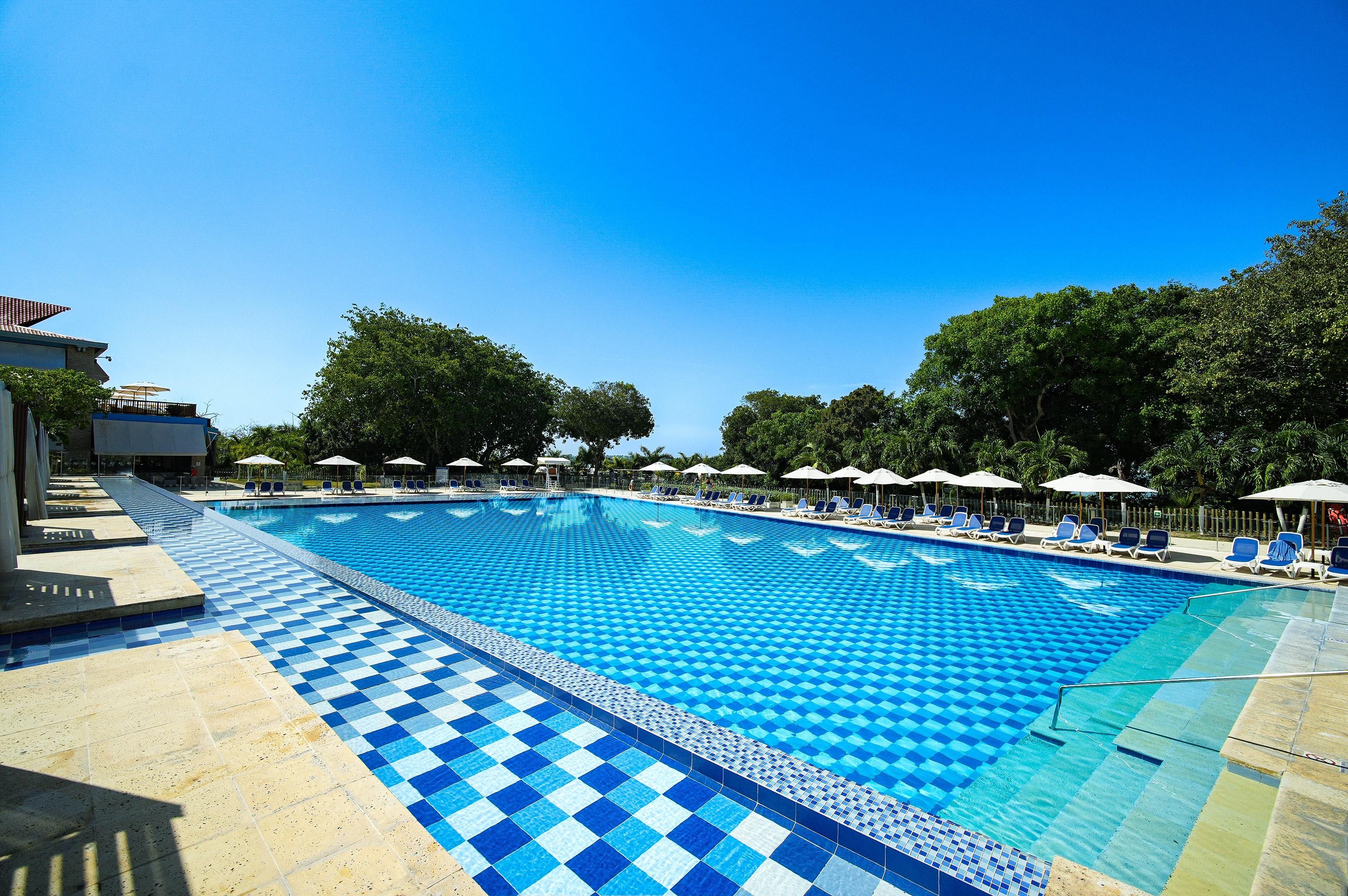 A large outdoor swimming pool with a checkered pattern, surrounded by lounge chairs and umbrellas.
