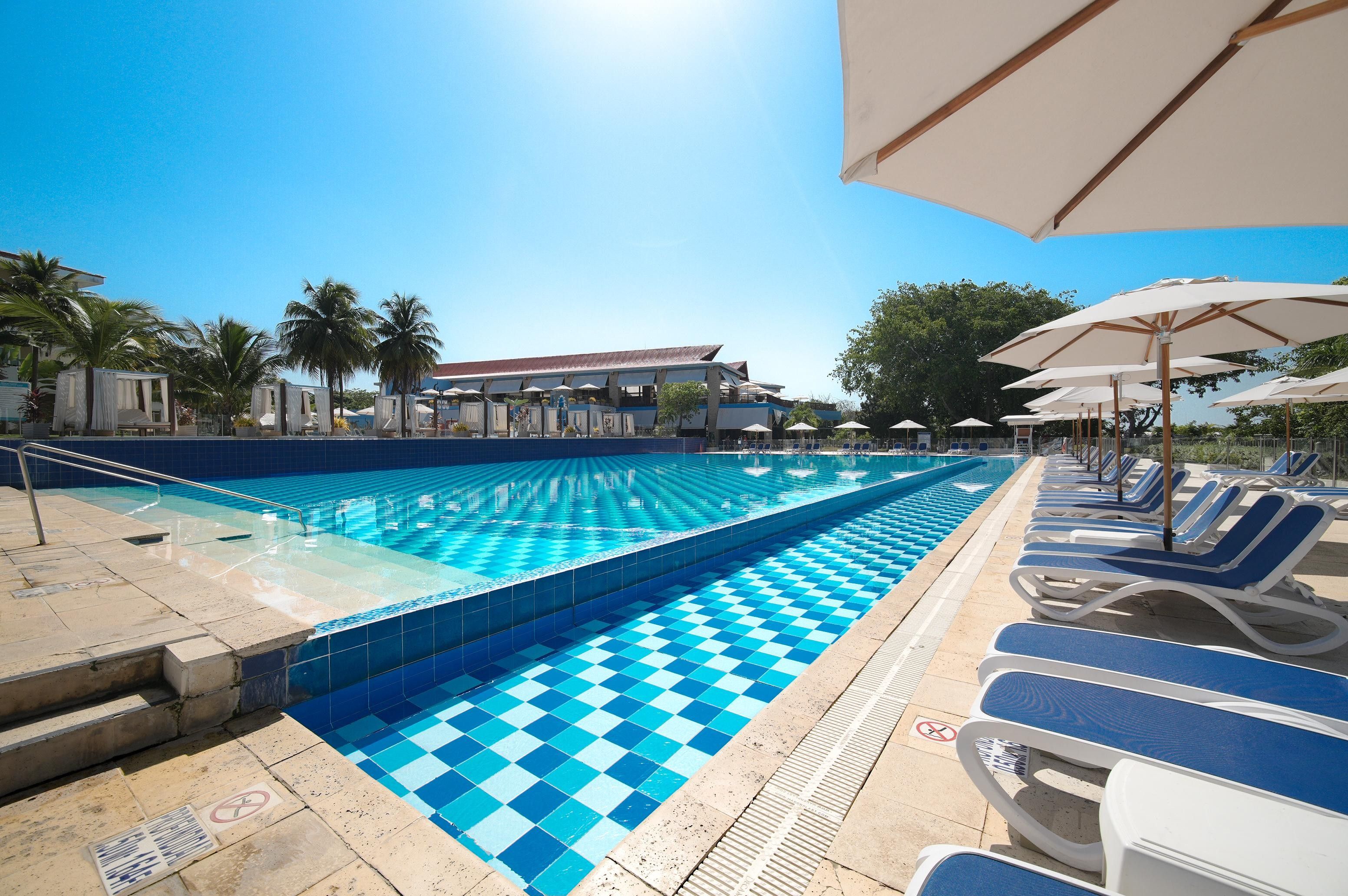 A swimming pool with a checkered pattern, lounge chairs, and umbrellas.