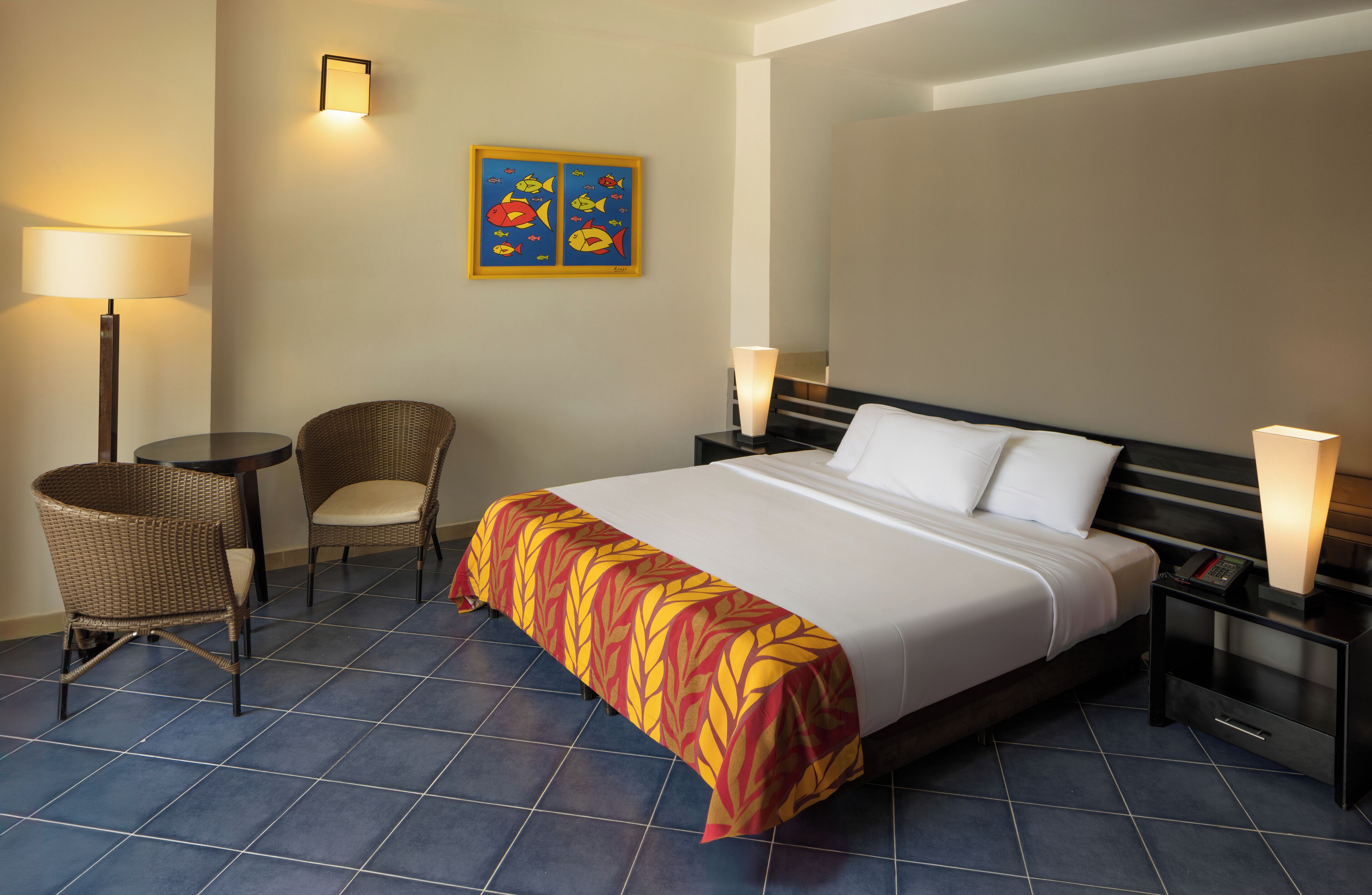 Ein Hotelzimmer mit einem großen Bett, zwei Nachttischen, einem Sessel, einer Lampe und einem Wandbild.