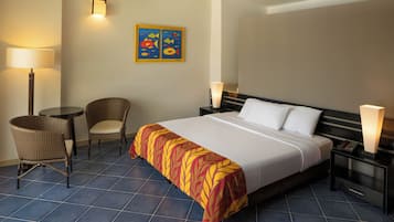 Ein Hotelzimmer mit einem großen Bett, zwei Nachttischen, einem Sessel, einer Lampe und einem Wandbild.