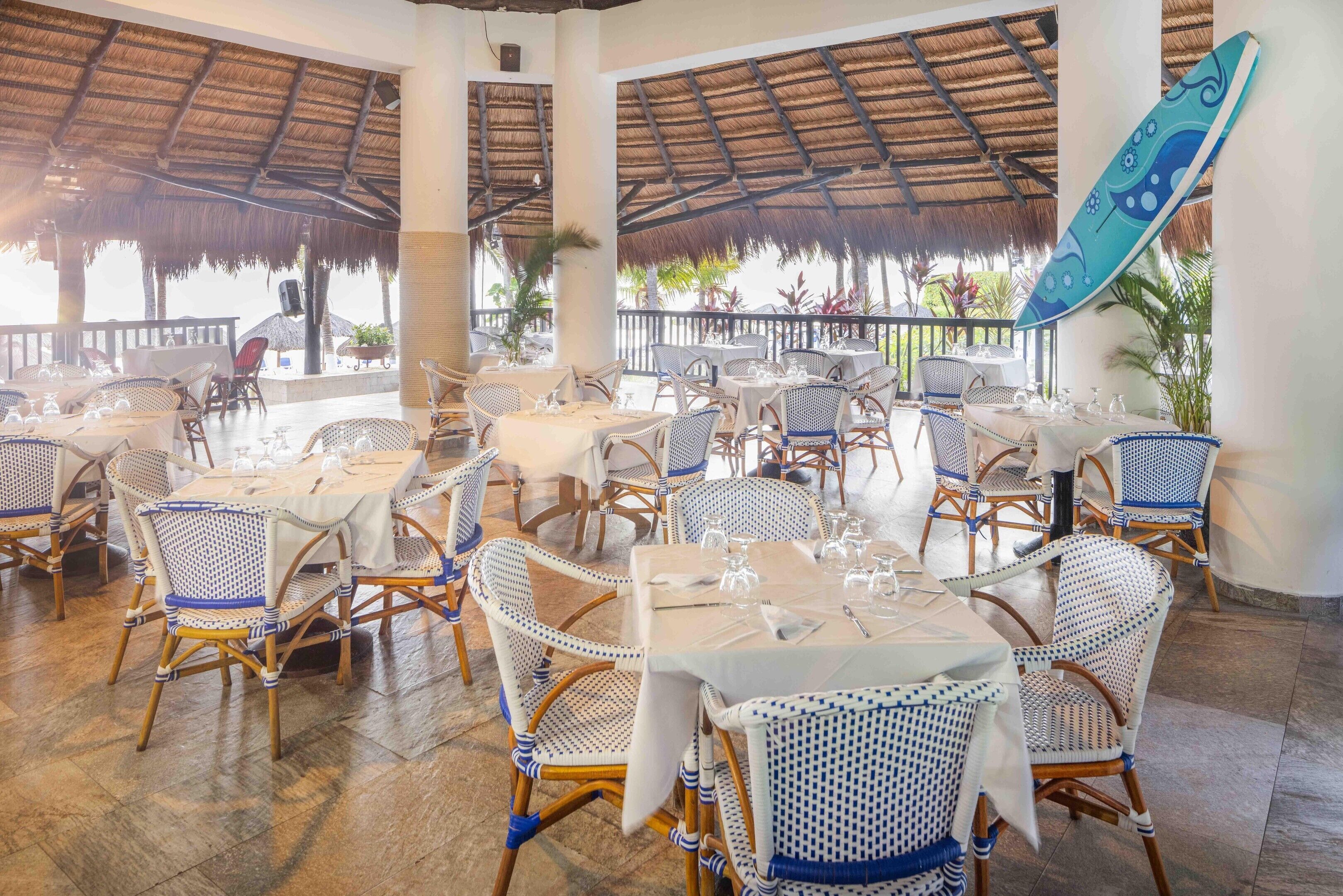 An outdoor restaurant with thatched roofs, wicker furniture, and tables set for dining.