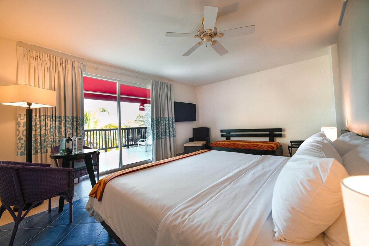 Quarto de hotel com cama, escrivaninha, cadeira, televisão e varanda com vista.