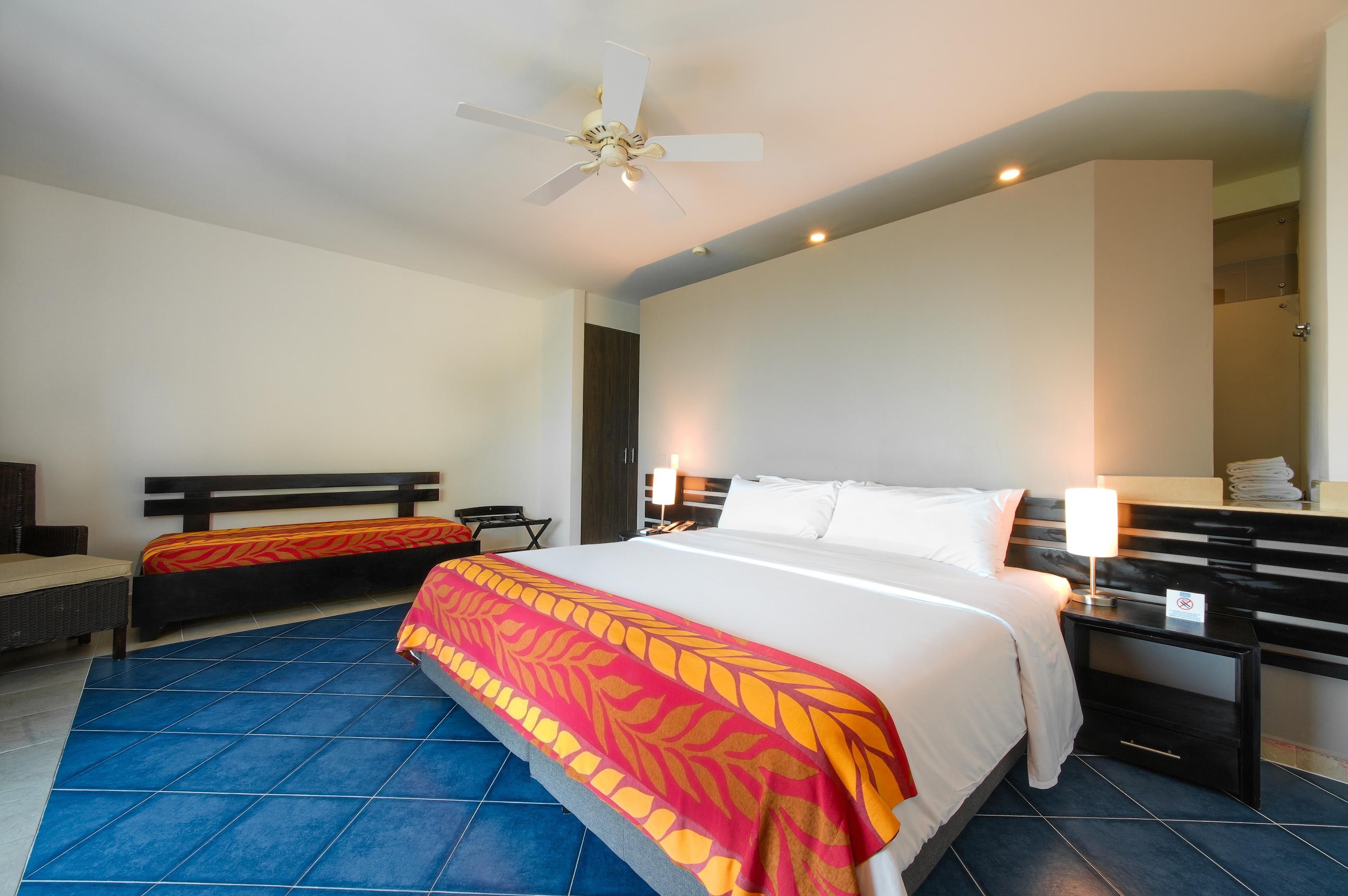 A hotel room with a bed, a chair, a desk, and a ceiling fan.