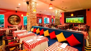 A restaurant with red and white striped tables, blue cushioned seating, and stone pillars. - Decameron Baru - All inclusive (Cartagena)