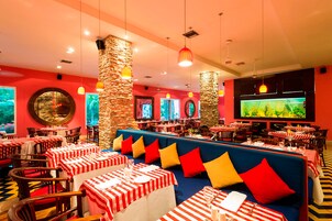 Un restaurante con mesas a rayas rojas y blancas, asientos acolchados en azul y pilares de piedra.