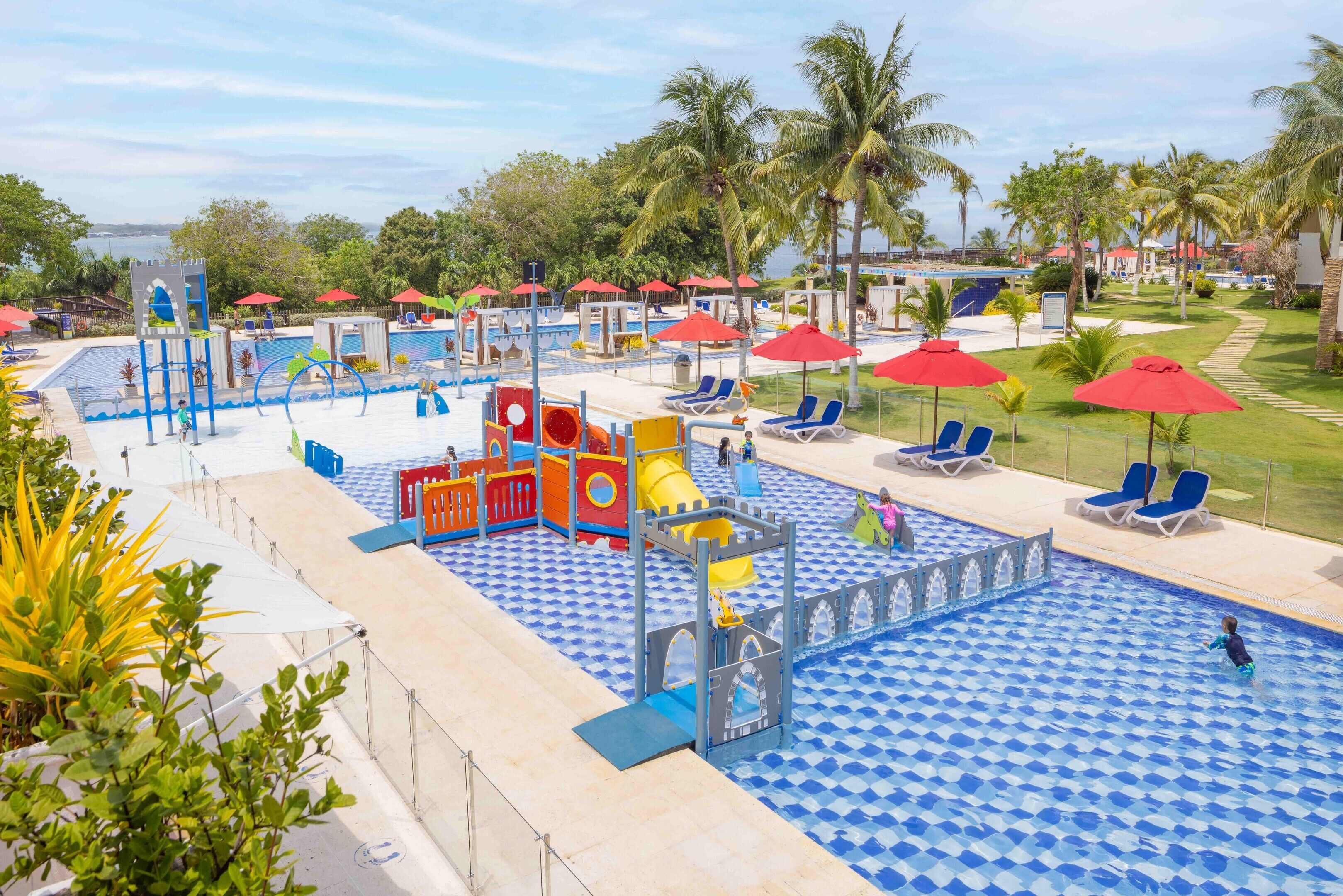 Ein Poolbereich mit Wasserspielanlage, Liegestühlen und Palmen.