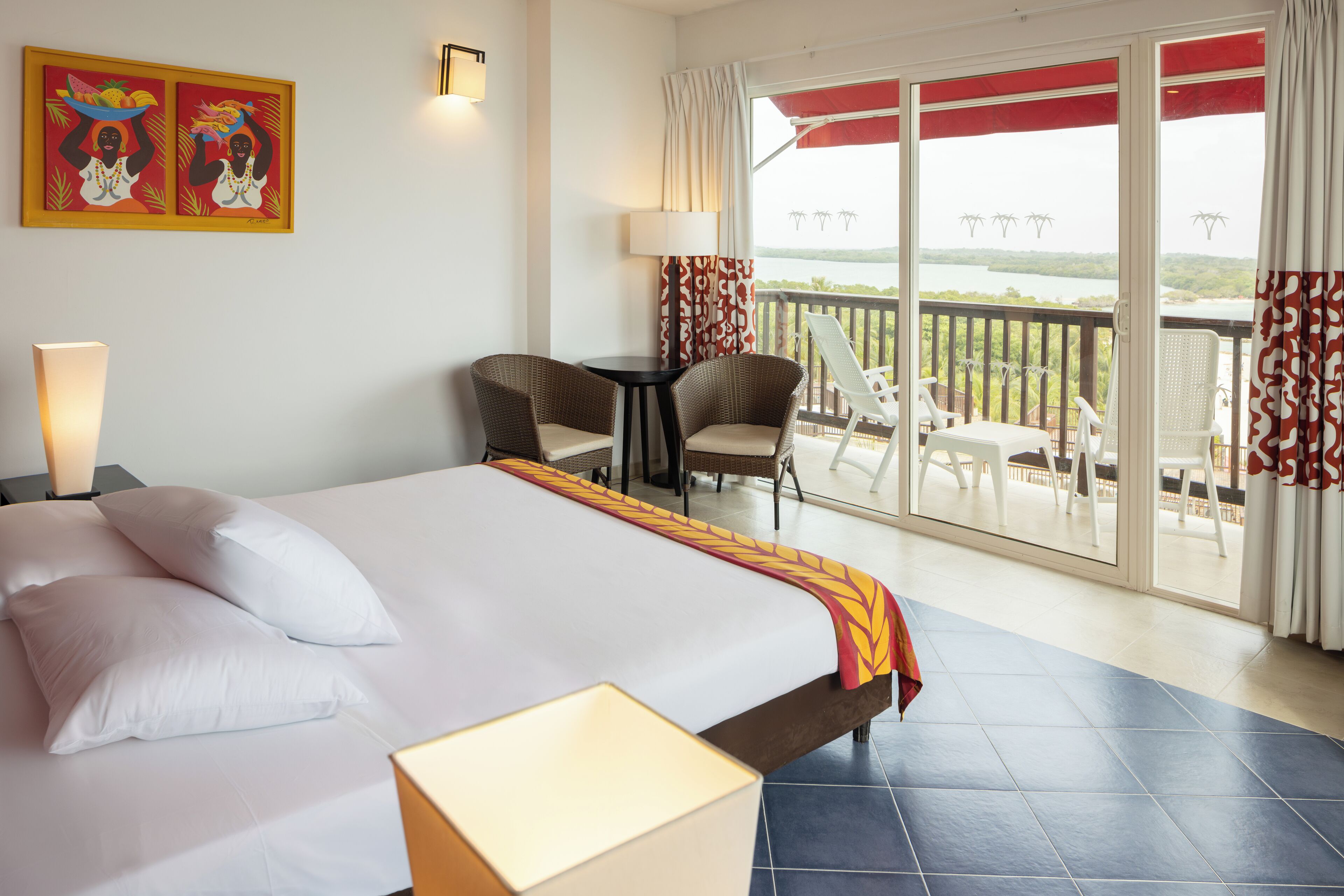A hotel room with a bed, a balcony with chairs, a table, and a view of a bridge.