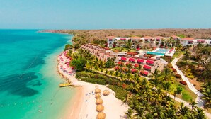 A resort with a beach, a pool, and multiple buildings with red roofs.
