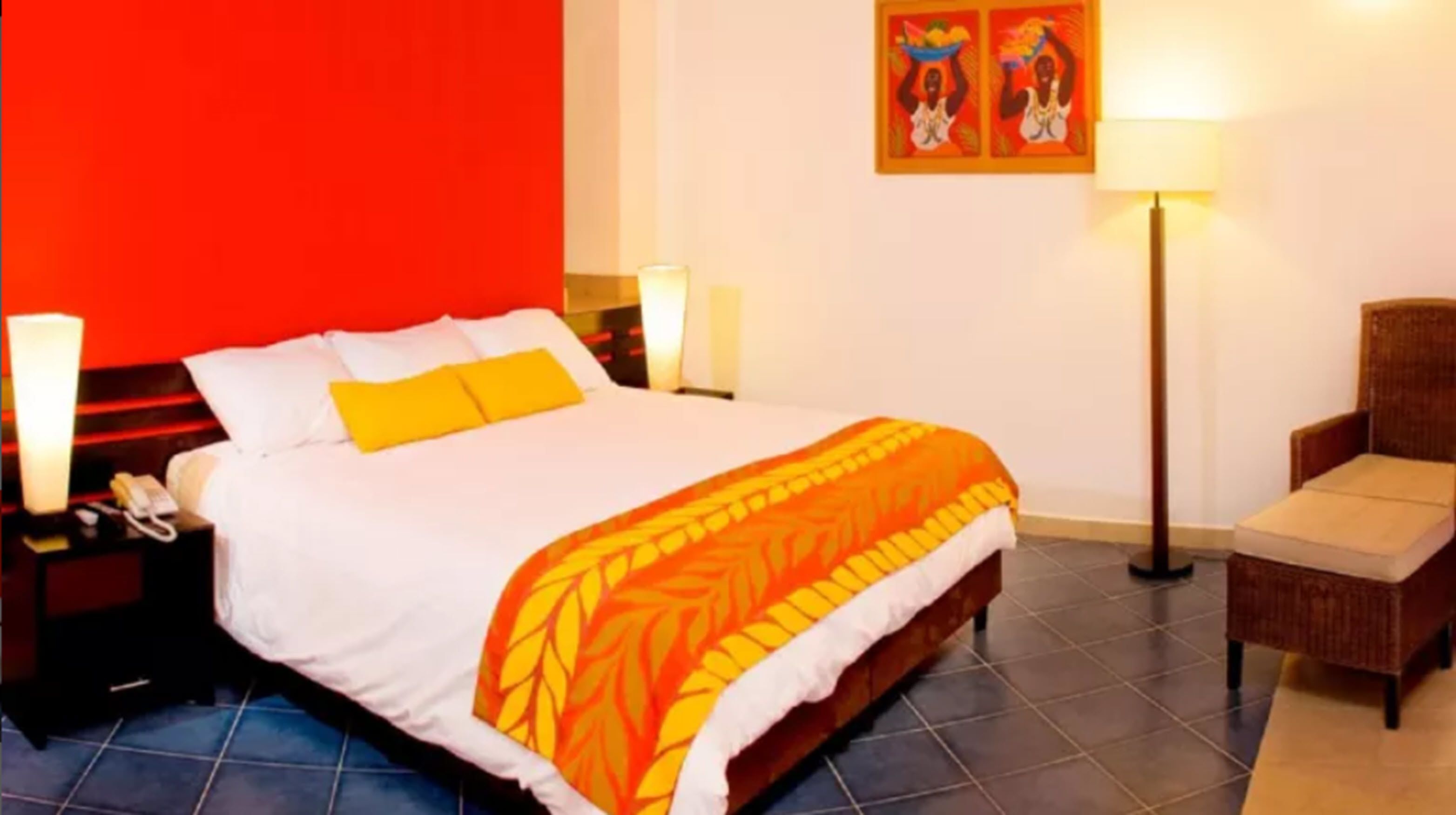 Habitación de hotel con cama, mesita de noche, una silla y dos lámparas fijadas a la pared.