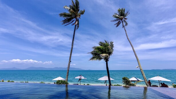 A poolside area with palm trees, umbrellas, and a view of the ocean. - Saree Samui Natures Finest Resort (Koh Samui)
