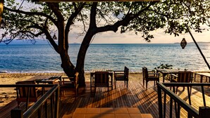 A wooden deck with tables and chairs overlooking a beach and the sea. - Saree Samui Natures Finest Resort (Koh Samui)