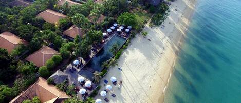 An aerial view of a resort with a pool, beach, and villas.