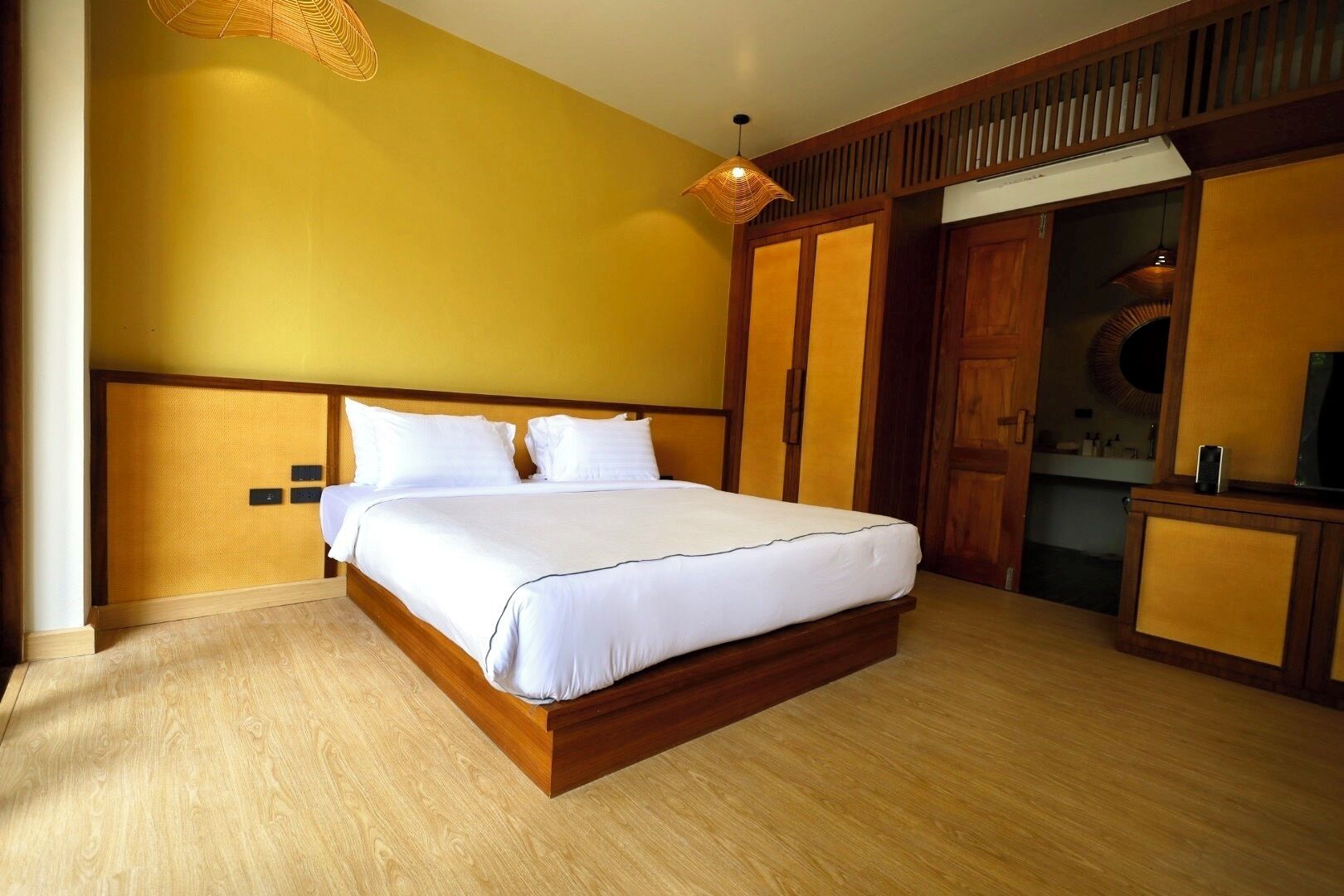 A hotel room with a large bed, wooden headboard, a hanging light fixture, and a wooden wardrobe.