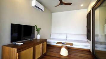 A modern living room with a flat-screen TV, wooden cabinet, potted plant, white sofa, and a ceiling fan.