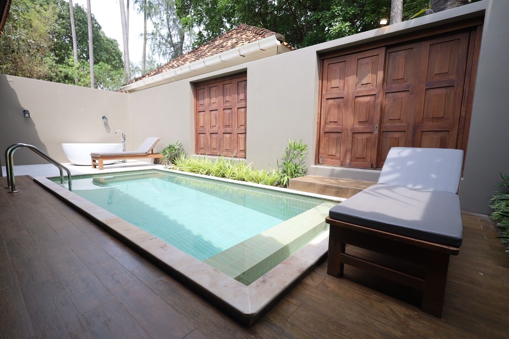 A swimming pool with a wooden deck, a lounge chair, and a small table.