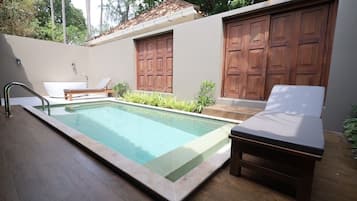 A swimming pool with a wooden deck, a lounge chair, and a small table.