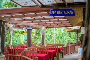 Un restaurante al aire libre con mesas y sillas rojas, una zona cubierta con techo de madera y un letrero que dice 'SAFA RESTAURANT'.