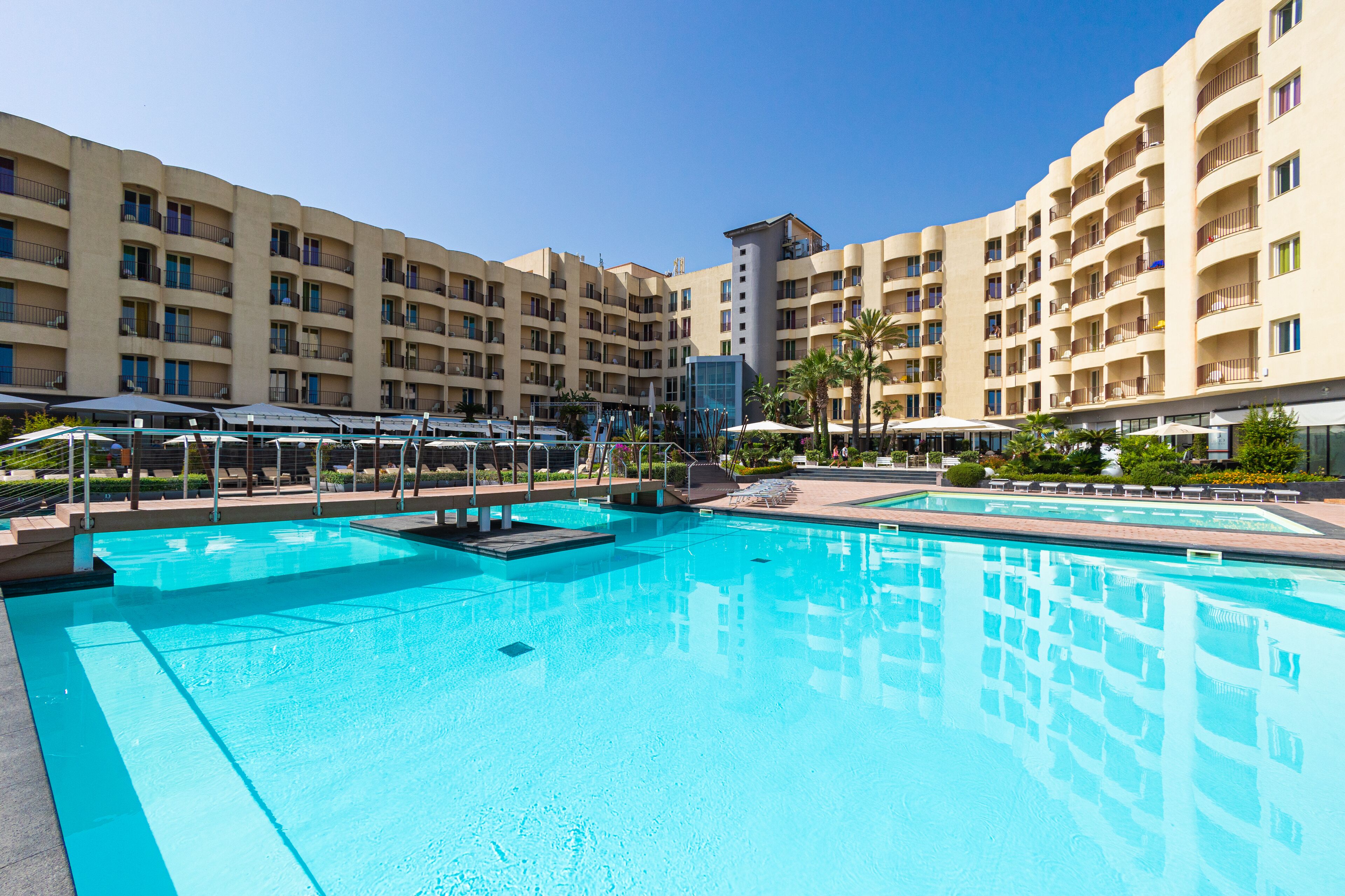 A hotel with multiple balconies, a swimming pool, and a clear blue sky.