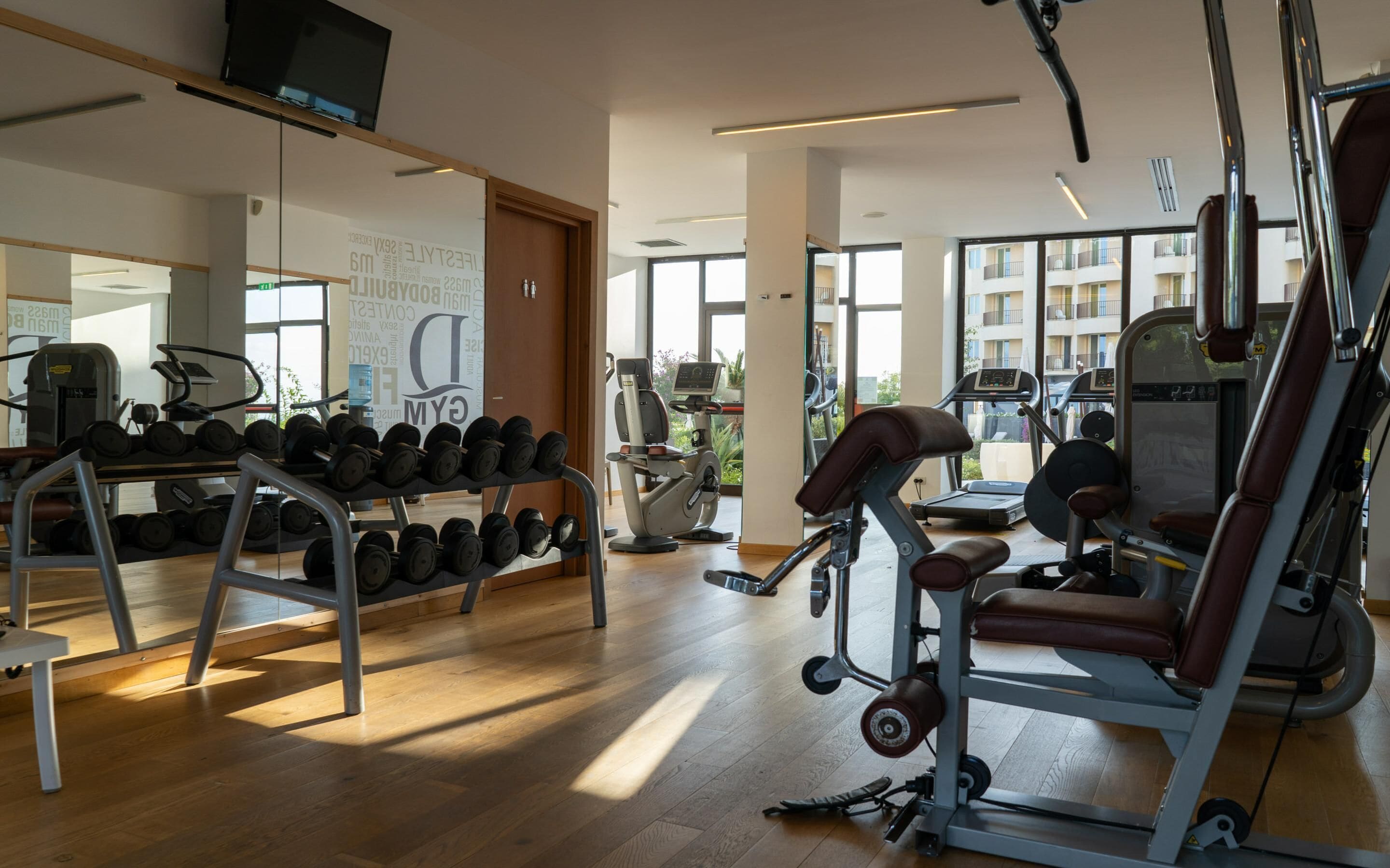 A gym with exercise equipment, a mirror, and a wooden floor.
