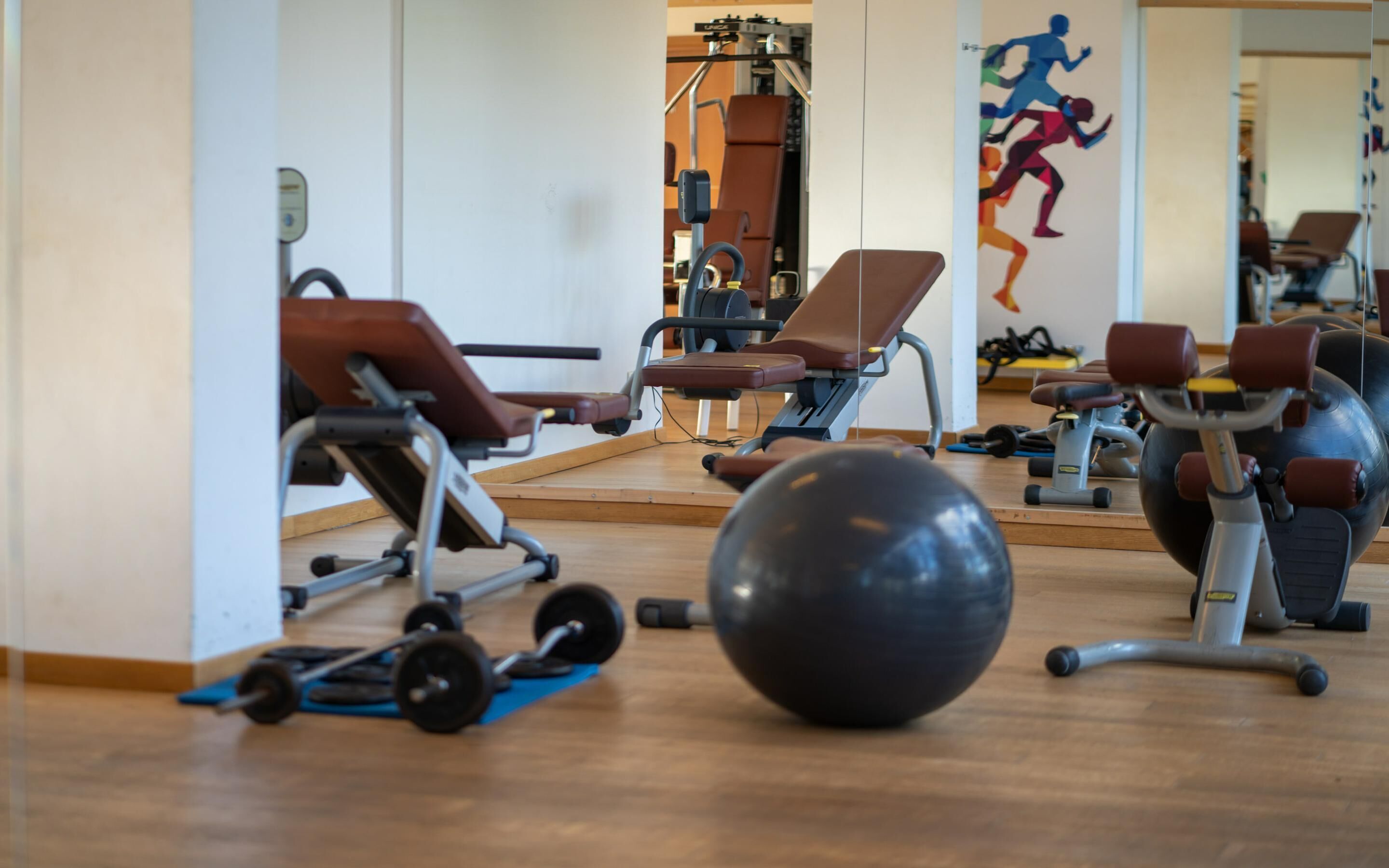 Un gimnasio con equipo de ejercicio, una pelota de ejercicio grande y un mural de corredores.