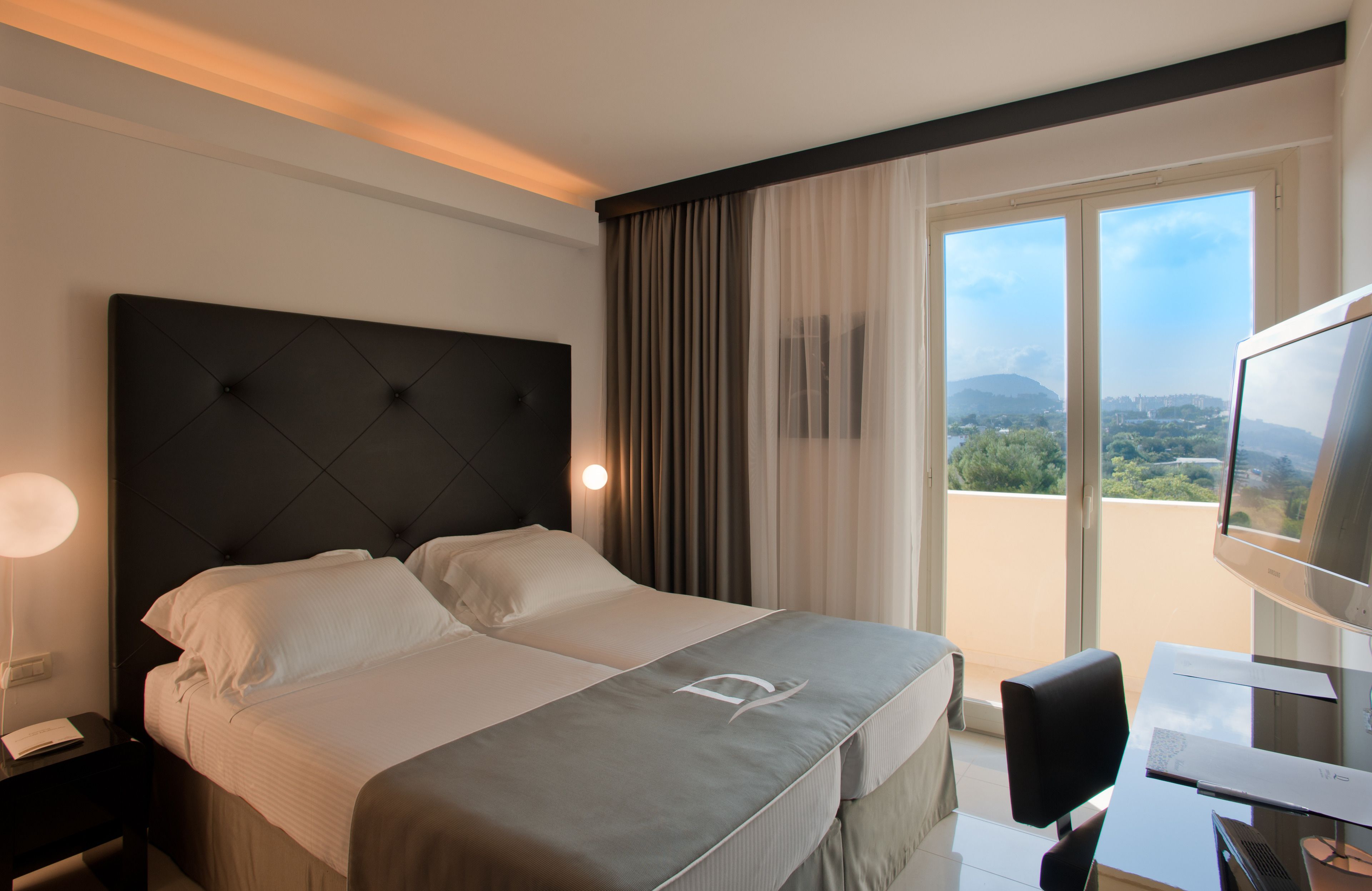 Habitación de hotel con una cama grande, un escritorio con computadora, un televisor y vistas al exterior.