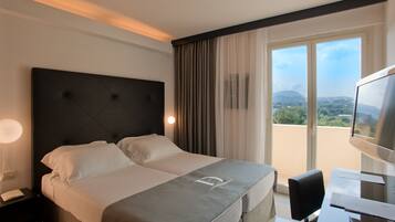 Habitación de hotel con una cama grande, un escritorio con computadora, un televisor y vistas al exterior.