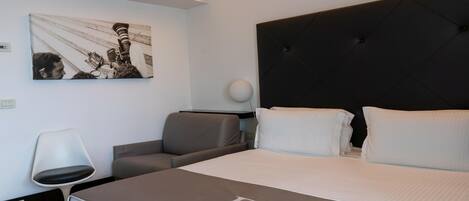 A modern hotel room with a large bed, a headboard, a desk, a chair, and a wall-mounted artwork.