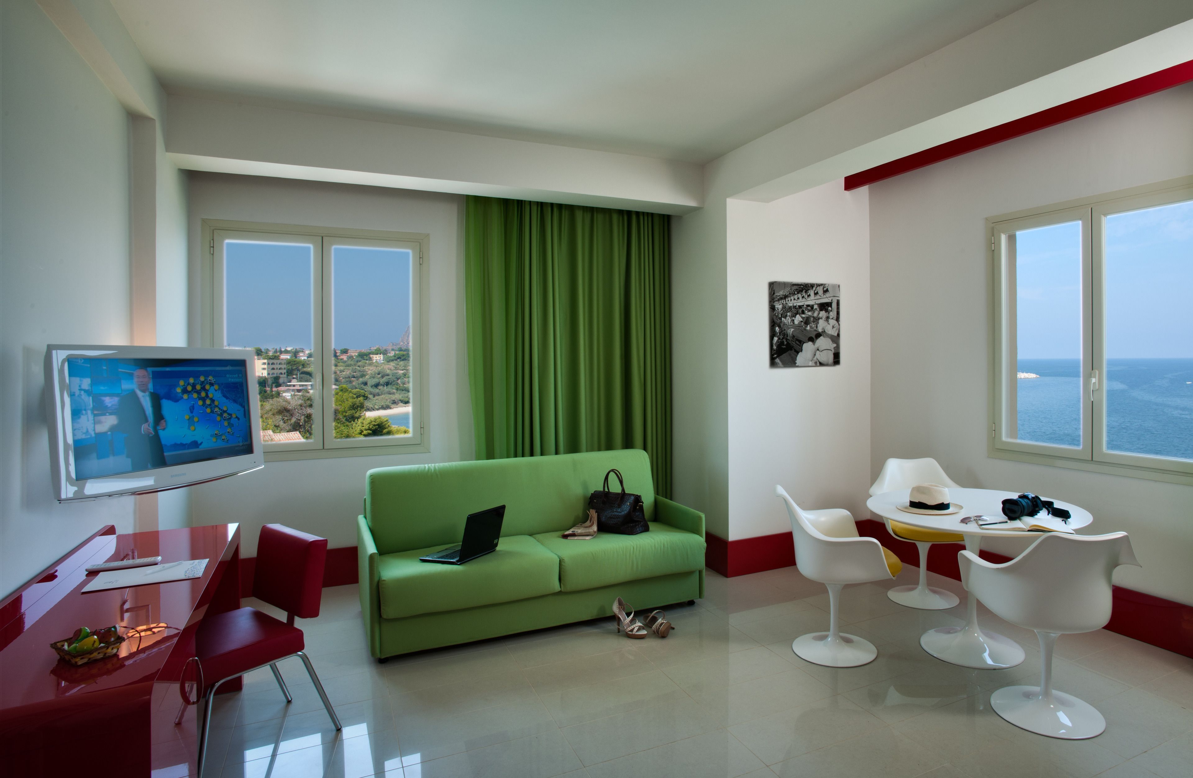 Et moderne hotelværelse med en grøn sofa, et spisebord med stole, et fjernsyn og havudsigt.