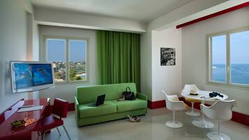 Et moderne hotelværelse med en grøn sofa, et spisebord med stole, et fjernsyn og havudsigt.