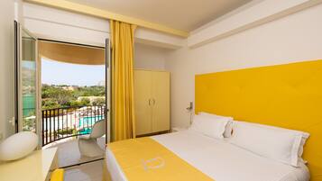 A hotel room with a bed, a desk, a chair, and a view of a pool and greenery.