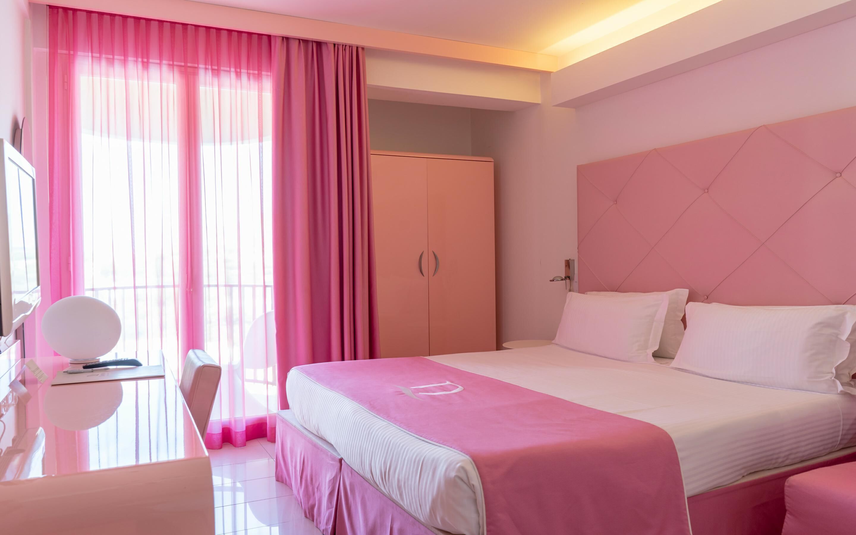 Habitació d'hotel amb un llit, una taula de treball, una cadira i un armari.