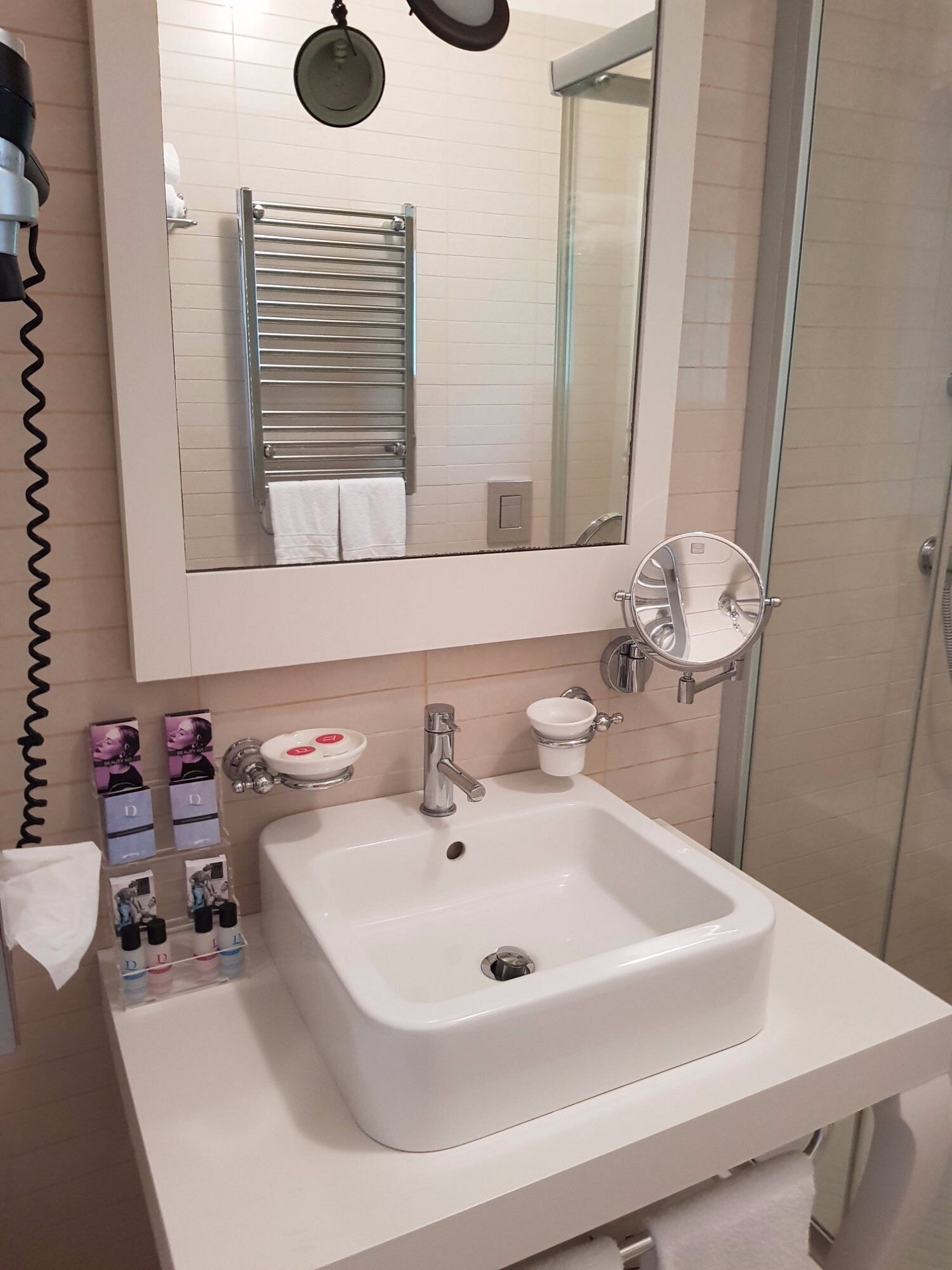 Une salle de bain avec un lavabo blanc, un miroir, un porte-serviettes et une cabine de douche en verre.