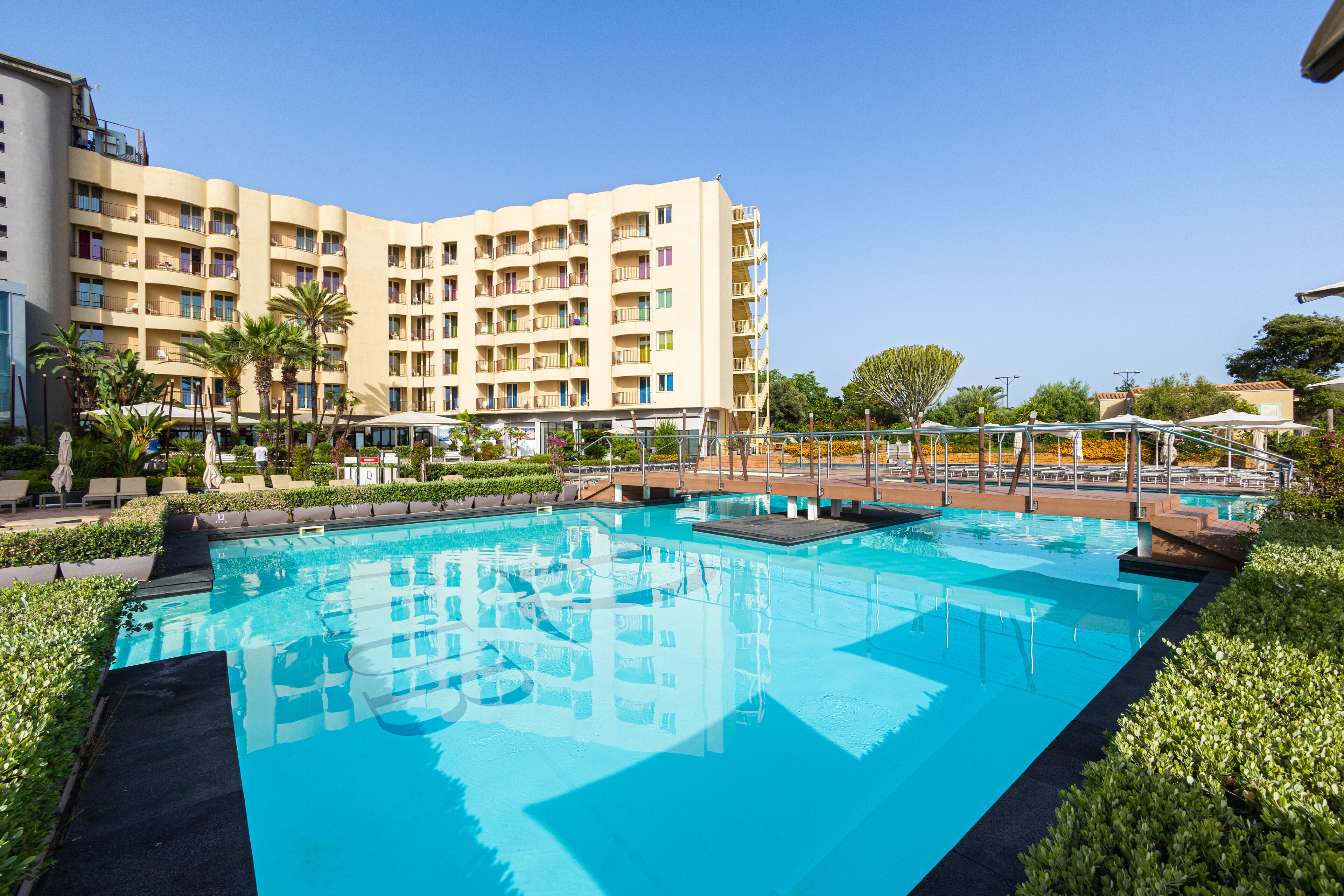 A hotel with a large swimming pool, multiple balconies, and lush landscaping.