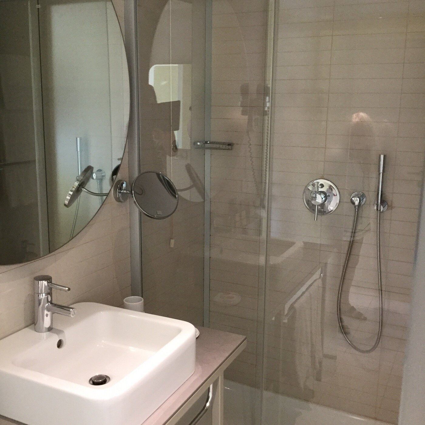A bathroom with a white sink, a mirror, a glass shower enclosure, and a handheld showerhead.