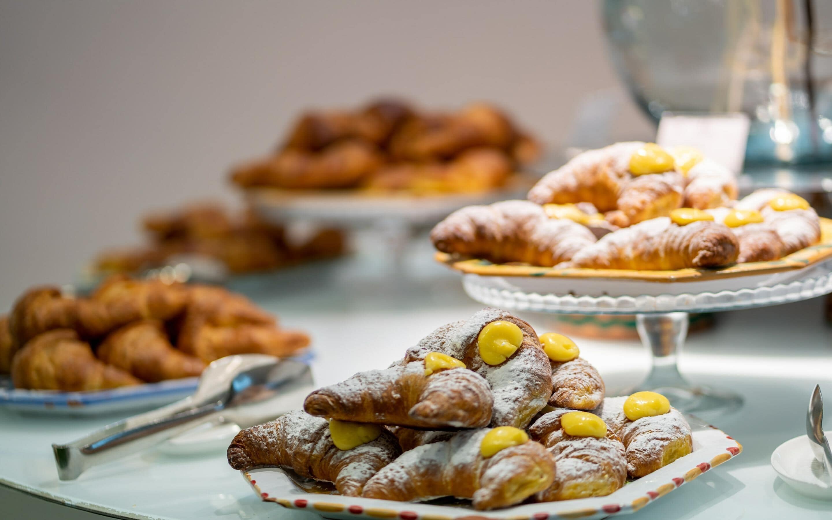 A variety of pastries on display, including croissants and cream puffs, arranged on plates and a stand.