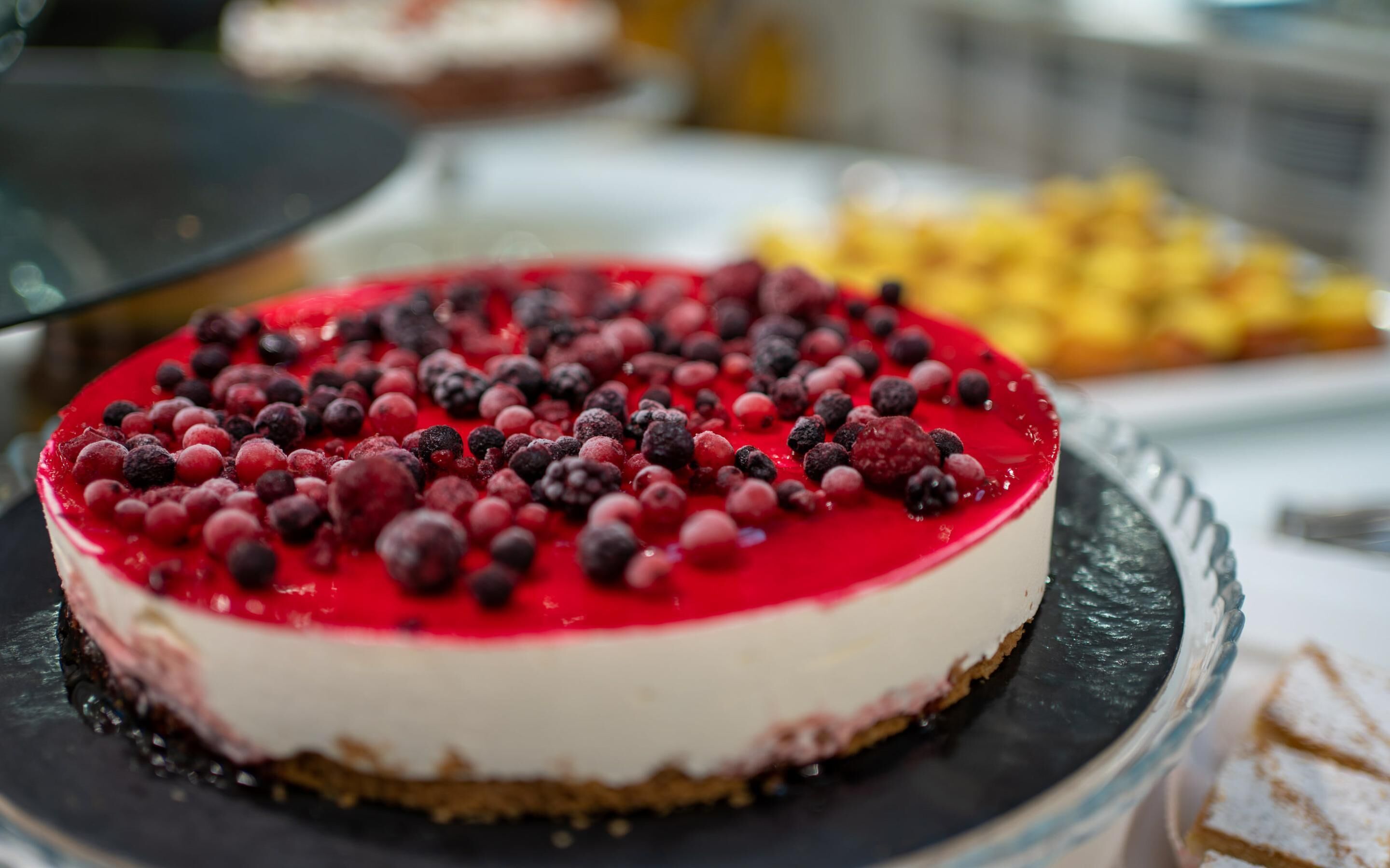 A cheesecake with a red topping and berries on a black plate.