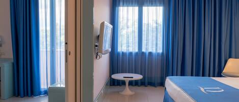A hotel room with a bed, a small table, a TV, and a window with curtains.