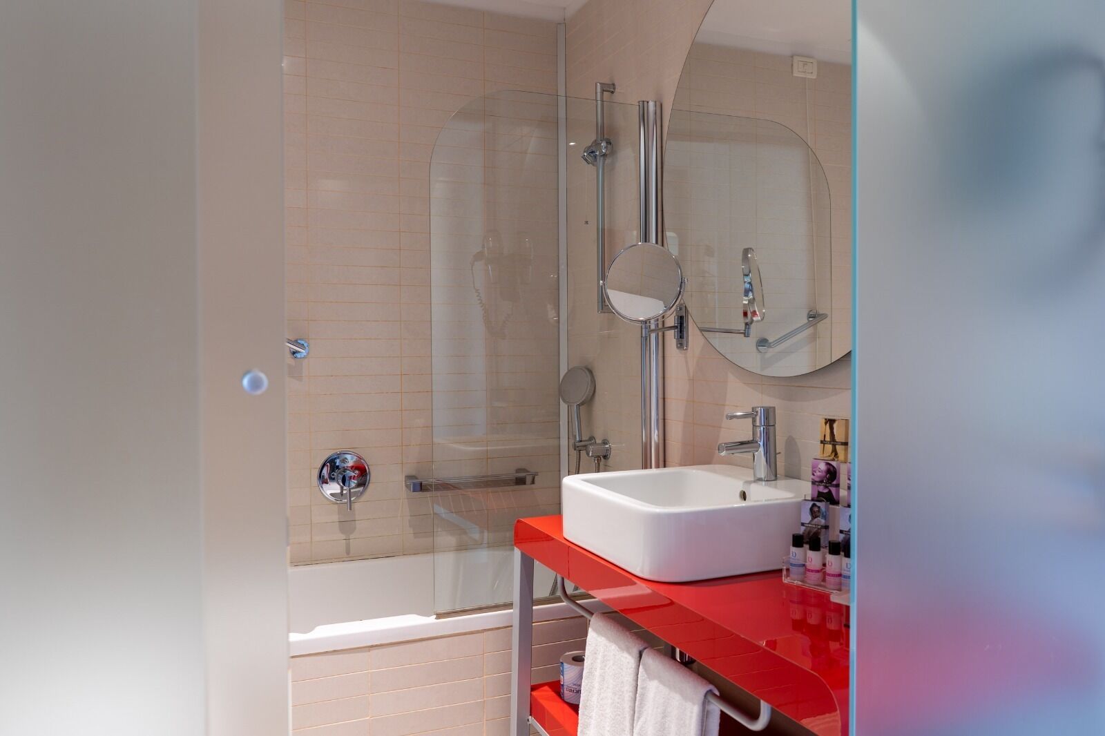 A modern bathroom with a glass shower enclosure, a white sink, and a red countertop.