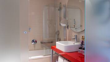 Un baño moderno con cabina de ducha de vidrio, lavamanos blanco y encimera roja.